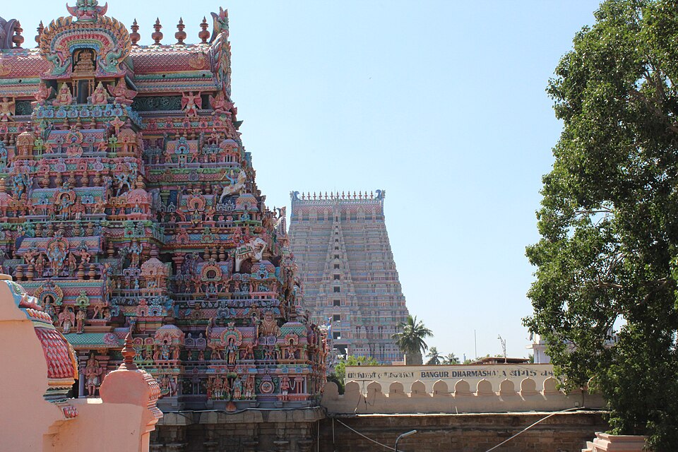 A brightly painted gopuram of the Srirangam Ranganathaswamy temple crowded with sculpted figures, with the tall pale Rajagopuram rising behind it