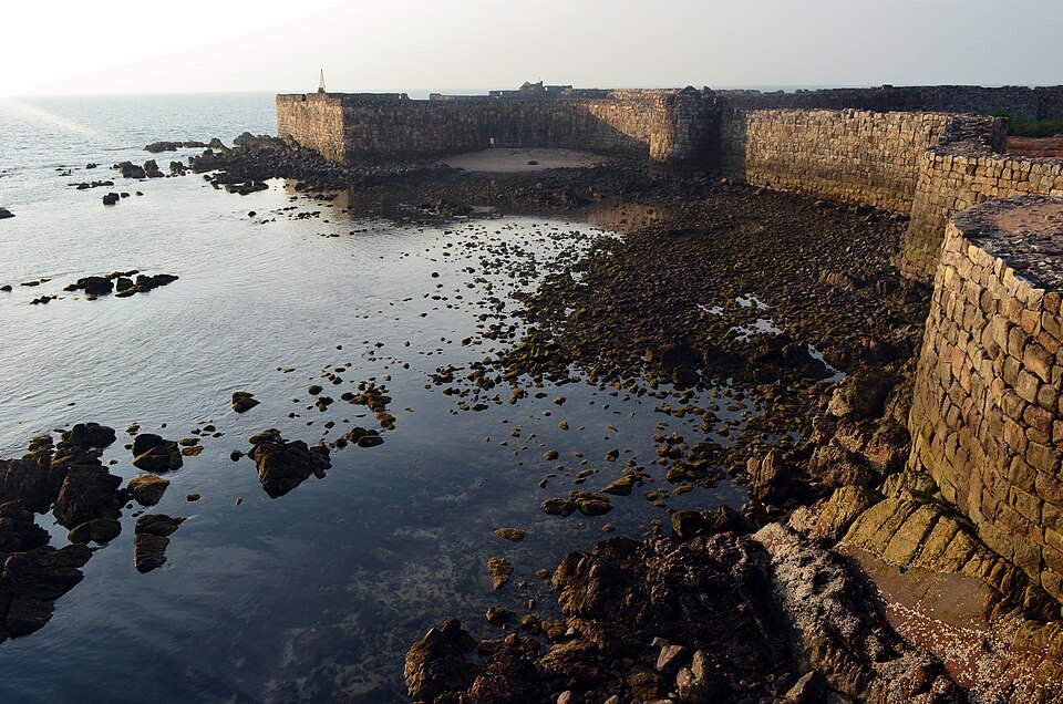The thick stone ramparts of Sindhudurg sea fort curving around a rocky tidal shore, with the open sea beyond