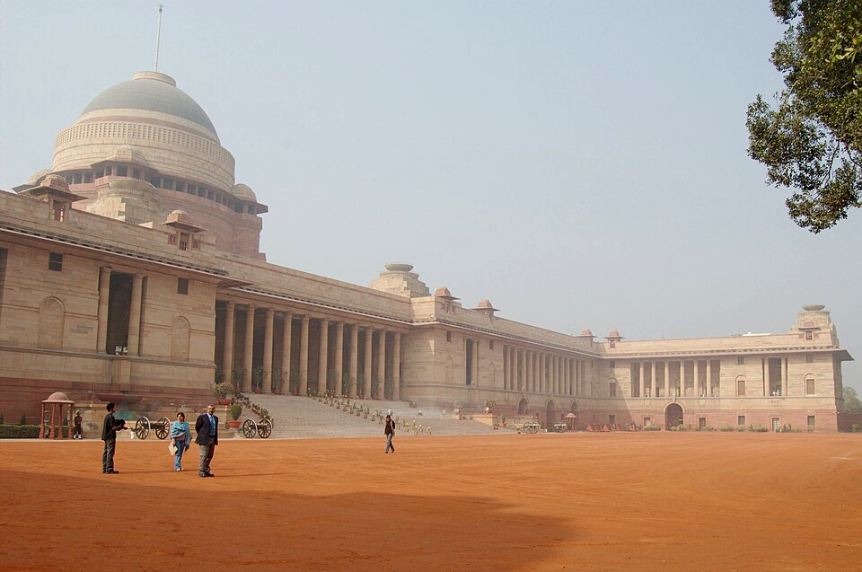 The long colonnaded front of Rashtrapati Bhavan in New Delhi, its broad ribbed dome rising above the sandstone facade across the red forecourt