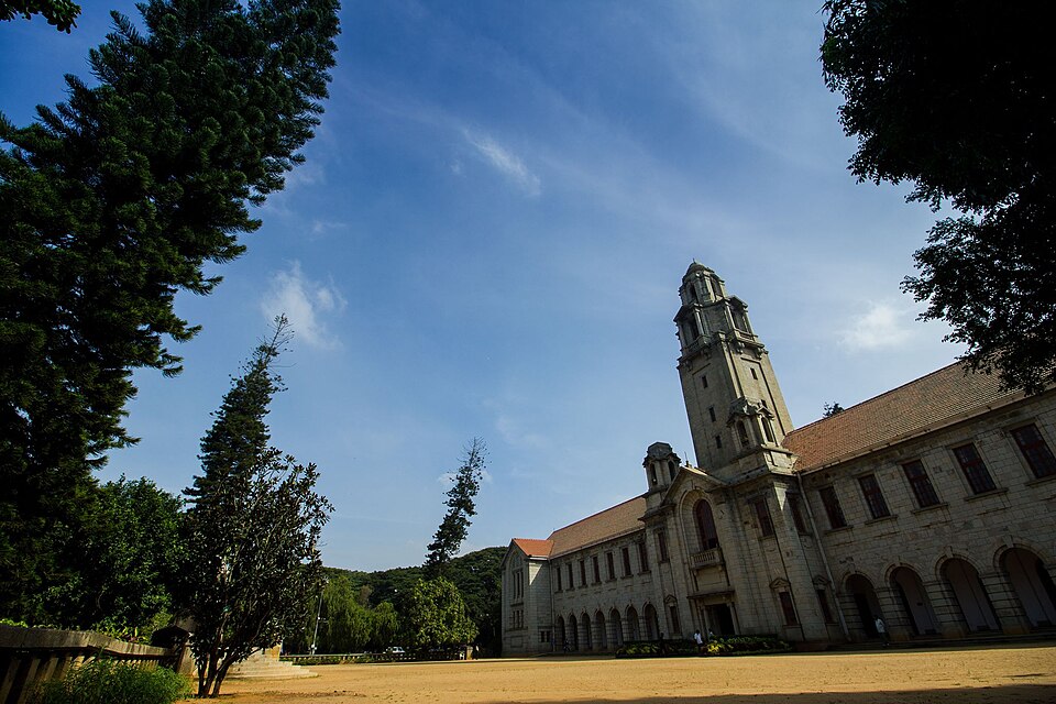 The stone Main Building of the Indian Institute of Science in Bengaluru, with its arcaded facade and tall clock tower against a blue sky