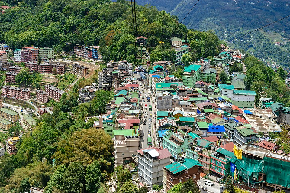 Aerial view of Gangtok, its green-roofed buildings packed along a steep forested Himalayan ridge with a road winding down the slope