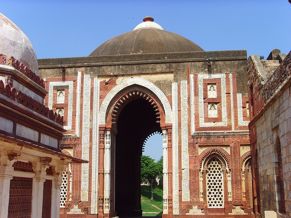 The Alai Darwaza in the Qutb complex, Delhi: a pointed arch with a lotus-bud fringe set in a red sandstone and white marble facade, with the low dome rising behind it