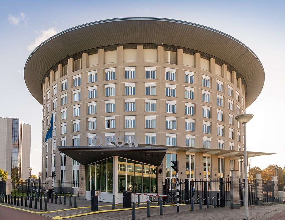 The curved, drum-shaped headquarters building of the OPCW in The Hague, with the letters OPCW mounted above its entrance canopy