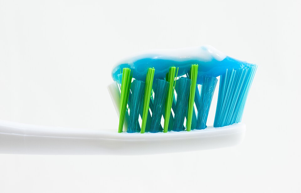 A close-up of a white toothbrush head whose blue and green bristles carry a ribbon of blue and white toothpaste.