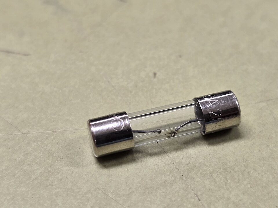 A glass cartridge fuse with metal end caps, its thin internal wire clearly melted through in the middle.