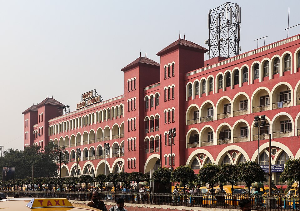 The red-and-white arcaded facade of Howrah Junction railway station in Kolkata, with the station nameboard reading Howrah.