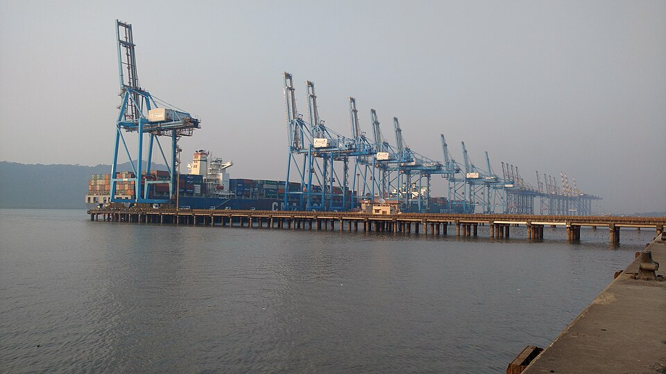 A row of blue gantry cranes lining the container quay at Jawaharlal Nehru Port, with a loaded container ship berthed alongside.