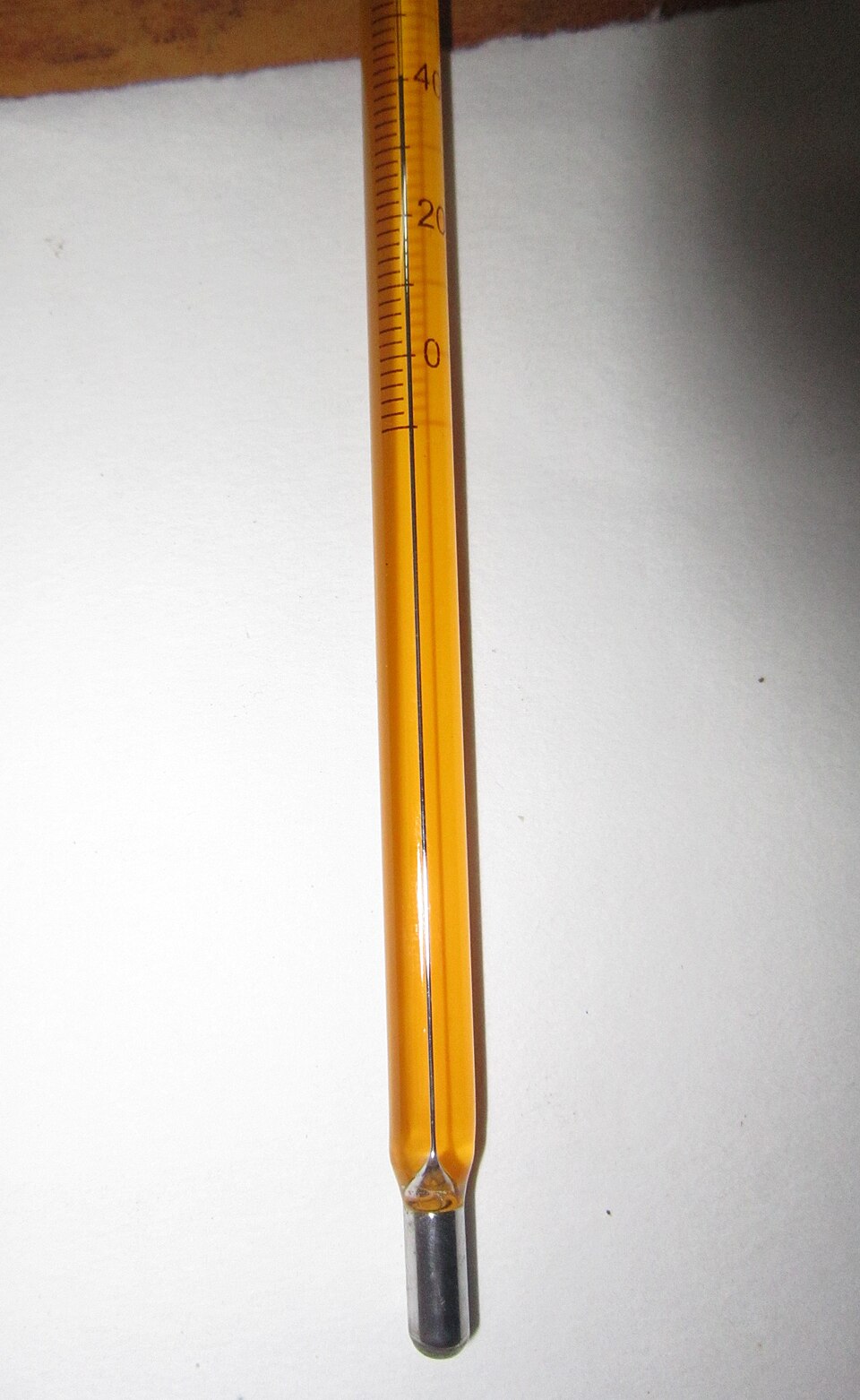 Close view of the lower end of a mercury-in-glass laboratory thermometer, showing the silver mercury bulb and the graduated scale marked in degrees.