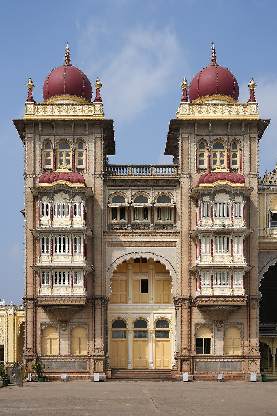 The front of the Amba Vilas Palace at Mysuru, showing two ornate towers capped with deep red domes flanking an arched entrance.
