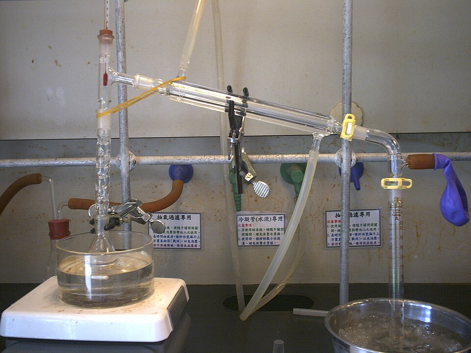 A laboratory distillation set-up: a flask of liquid heated in a bath, a fractionating column with a thermometer, and a water-cooled condenser leading the vapour down into a receiving cylinder standing in ice.