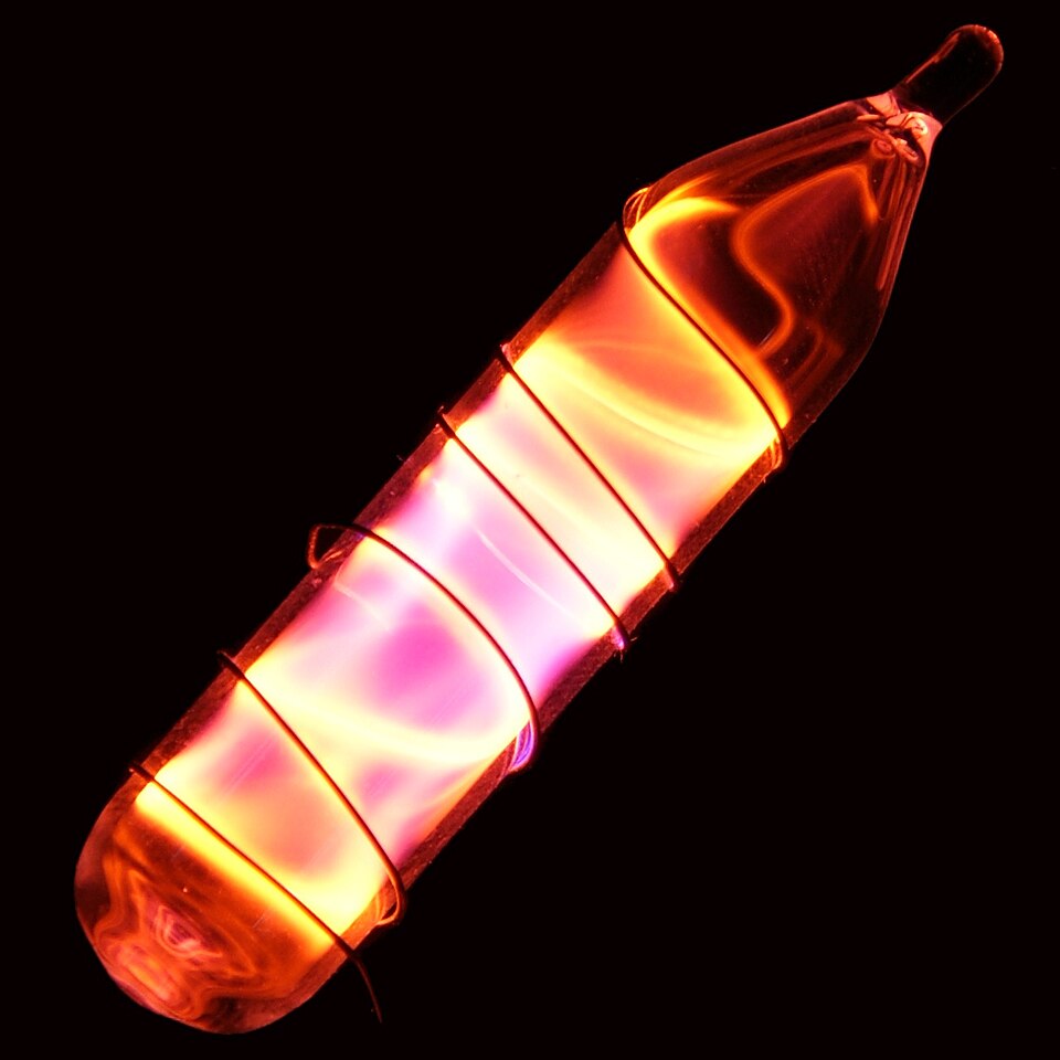 A sealed glass tube of neon gas glowing bright orange-red as an electric discharge passes through it, photographed against a black background.