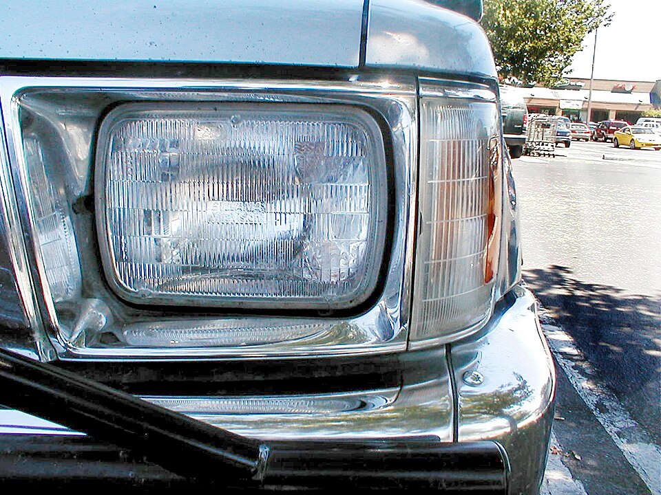 Close-up of a rectangular sealed-beam headlamp on a vehicle, its fluted glass lens showing the curved mirrored reflector and bulb set behind it.