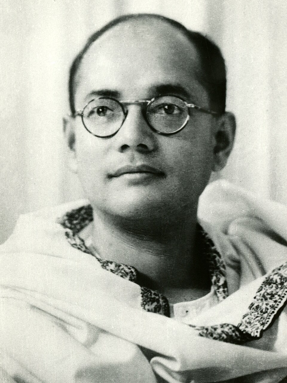 A black-and-white studio portrait of Subhas Chandra Bose in round spectacles, wearing a white kurta with an embroidered collar and a shawl over one shoulder.