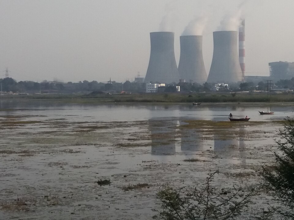 Three steaming cooling towers and a tall red-and-white chimney of the Koradi thermal power station near Nagpur, seen across the shallow water of Koradi Lake.