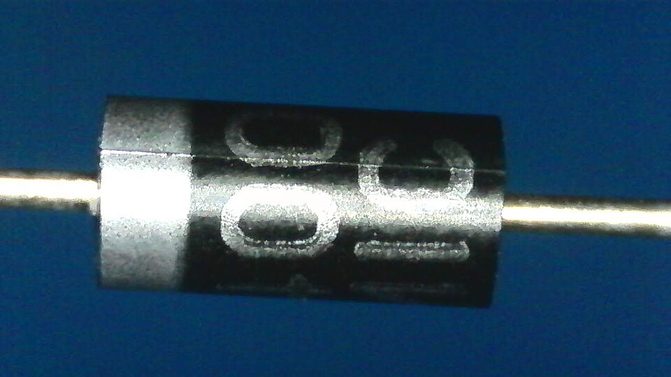 Close-up of a 1N4007 semiconductor rectifier diode, a small black cylinder with a white cathode band and a wire lead at each end.