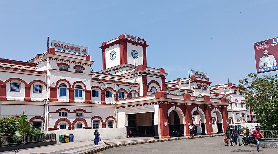 The red-and-white arcaded front facade of Gorakhpur Junction railway station under a clear sky, with a clock tower and a rooftop sign reading GORAKHPUR JN.