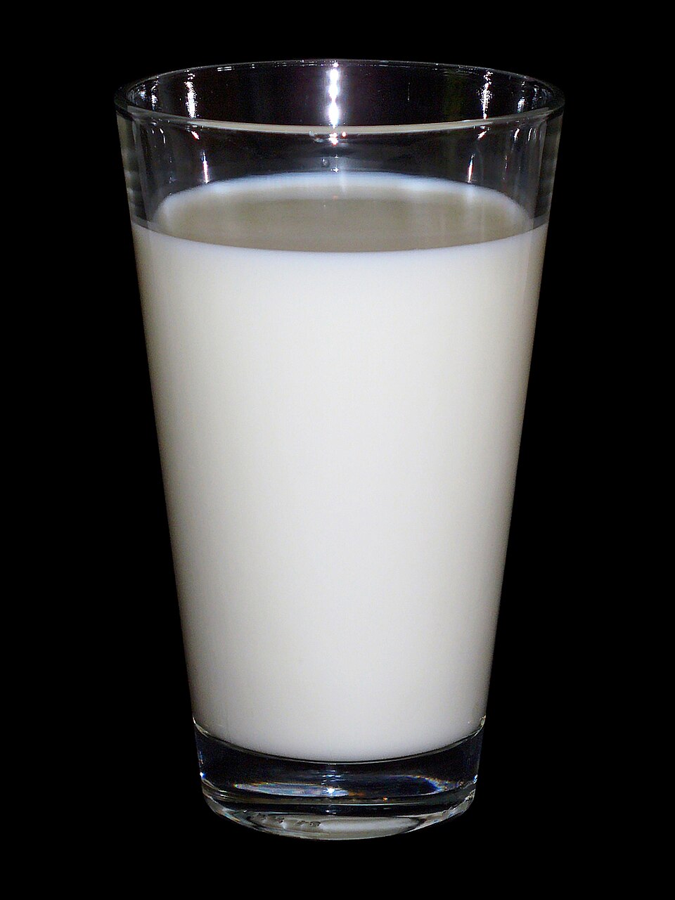 A tall clear drinking glass filled with white milk, photographed against a black background.