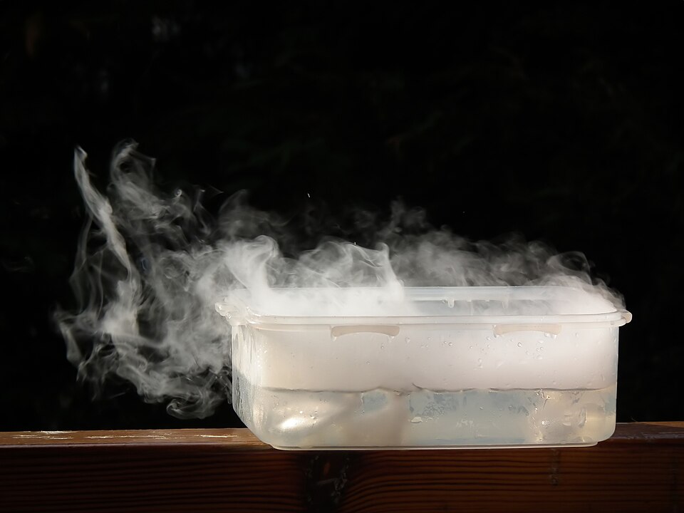 A plastic tub holding solid carbon dioxide, with thick white fog pouring over its rim as the dry ice turns straight into gas.