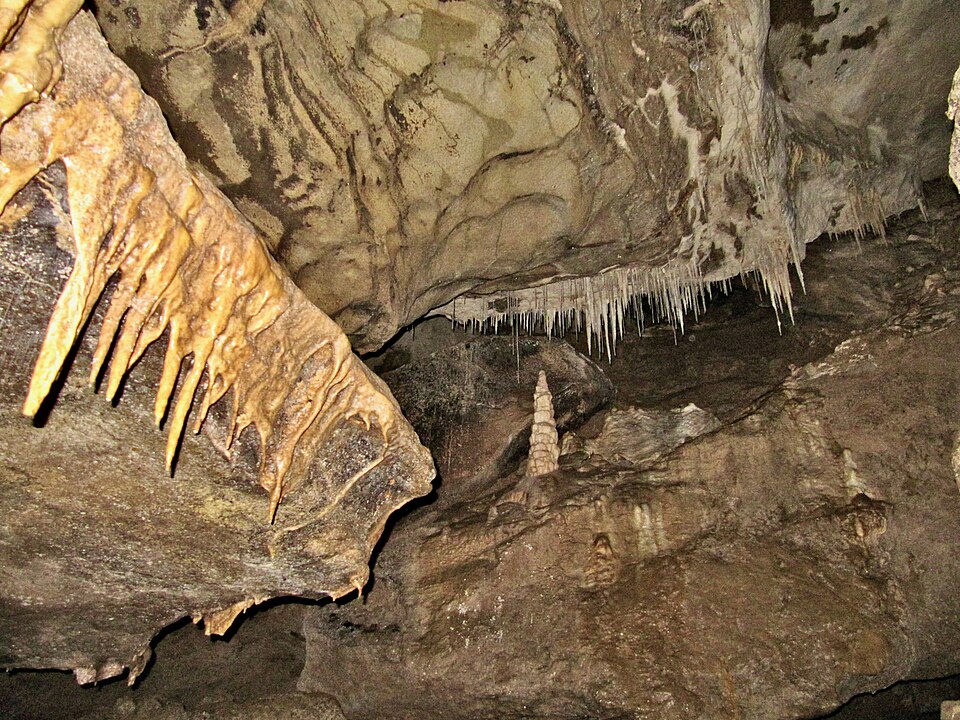 Stalactites hanging from the ceiling and stalagmites rising from the floor inside a limestone cave.