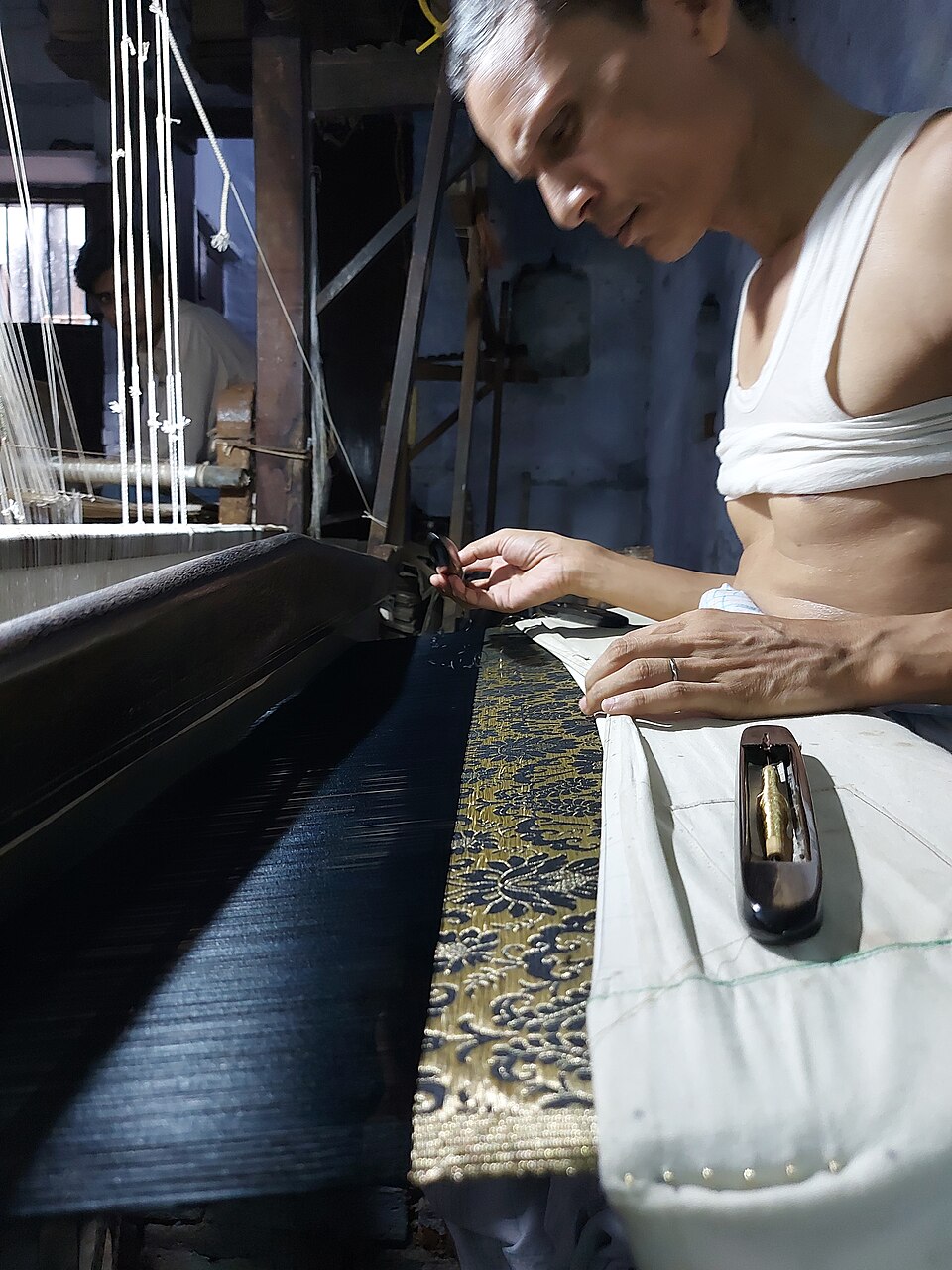 A handloom weaver working at his loom on a gold-brocade textile.