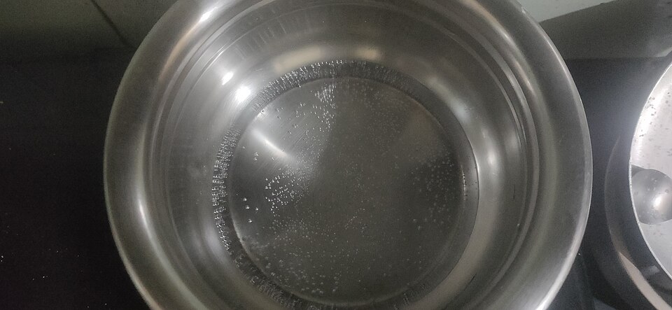 Water boiling in a metal pan, with vapour bubbles rising from within the liquid.