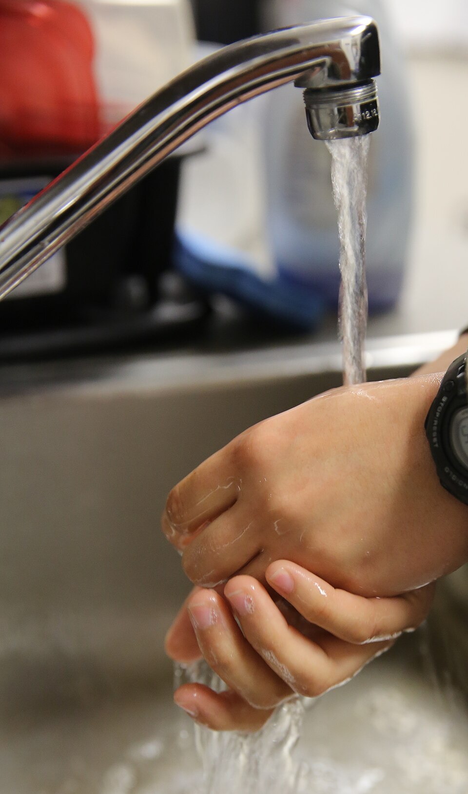 Hands lathered with soap under running water, the soap acting as a surfactant to lift dirt.
