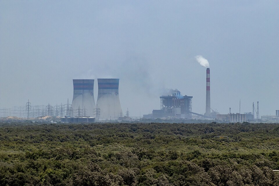 A coal-fired thermal power station with cooling towers and a tall chimney stack emitting a smoke plume