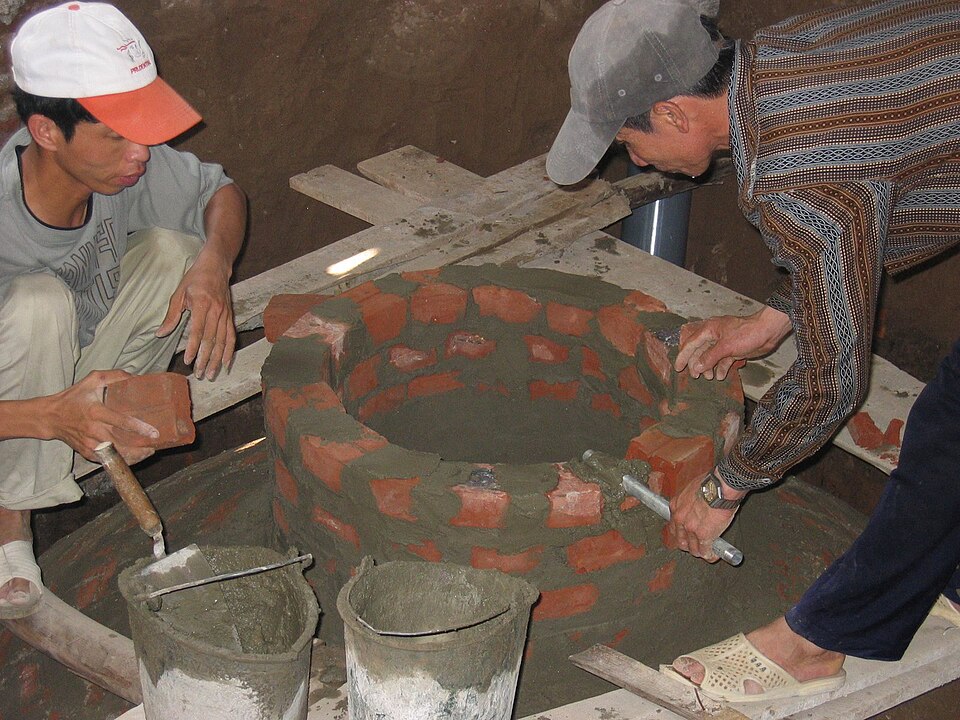 A fixed-dome biogas digester being built from brick, showing the dome-shaped chamber that converts dung into biogas