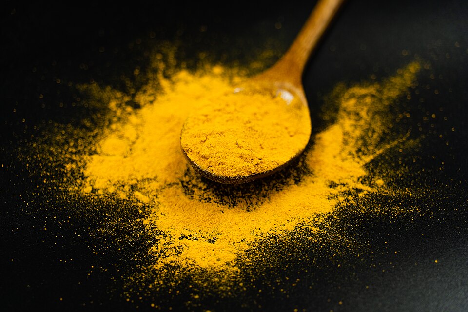 Bright yellow turmeric (haldi) powder on a wooden spoon, used as a natural acid-base indicator