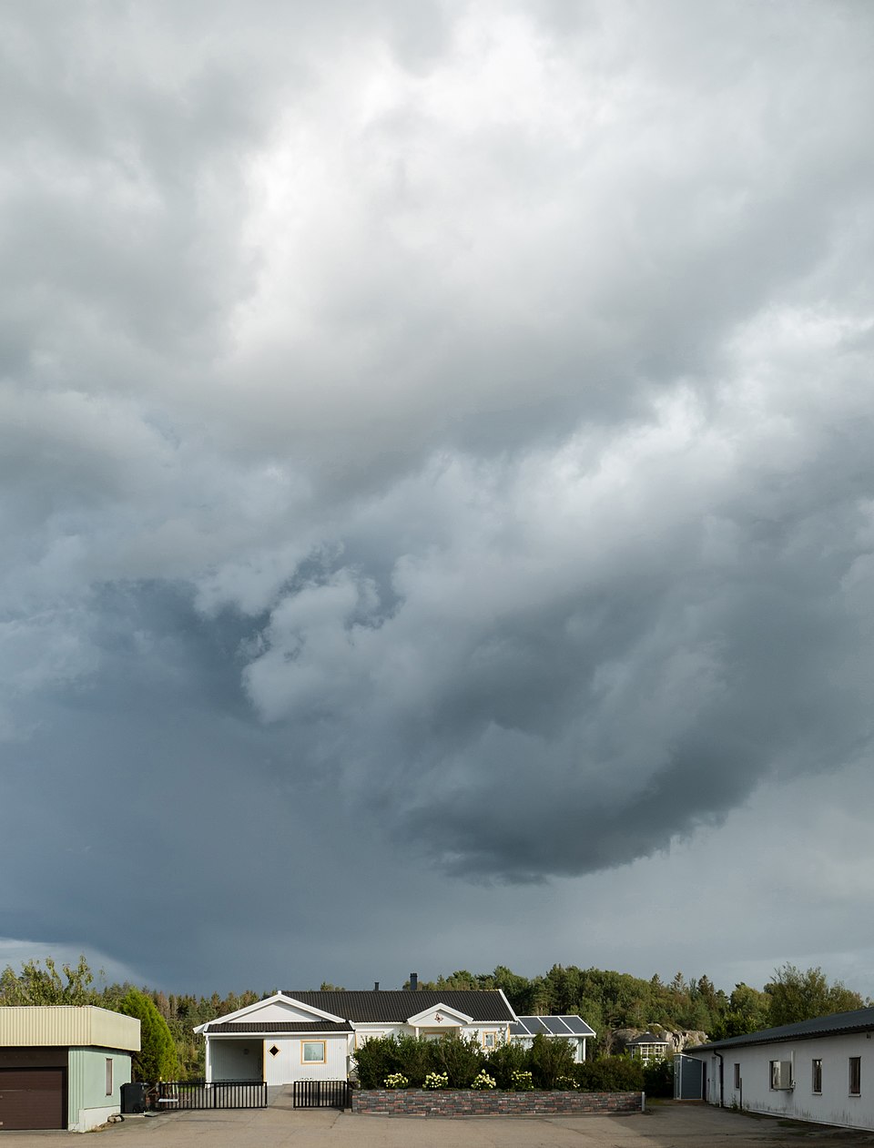 A heavy dark grey rain-bearing cloud looming over a village landscape at the edge of a rainstorm