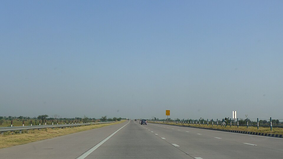 A wide multi-lane divided expressway in India with crash barriers stretching to the horizon