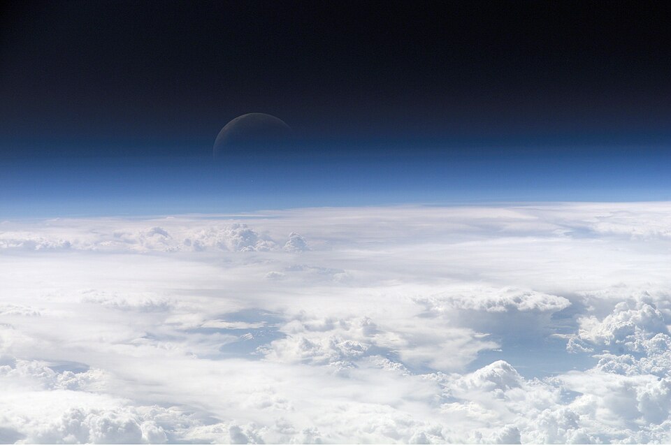 The thin blue arc of Earth's atmosphere photographed from orbit, with the crescent Moon above