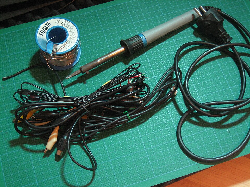 A reel of tin-lead solder wire beside a soldering iron