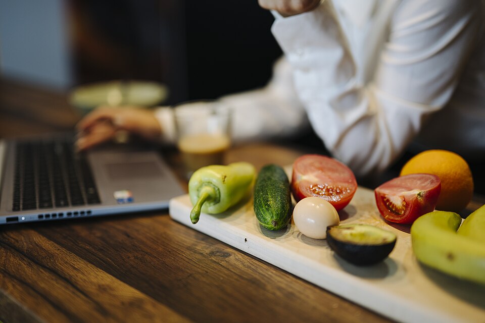 An assortment of fresh vegetables and fruits including peppers, cucumber, tomatoes, orange, banana and avocado