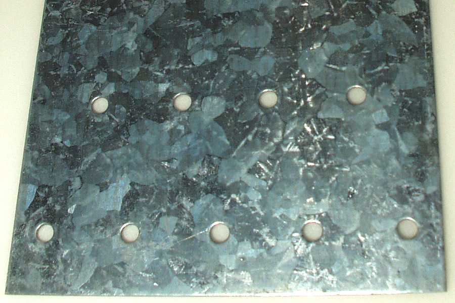 Close-up of a galvanised, zinc-coated steel sheet showing the characteristic crystalline spangle pattern.