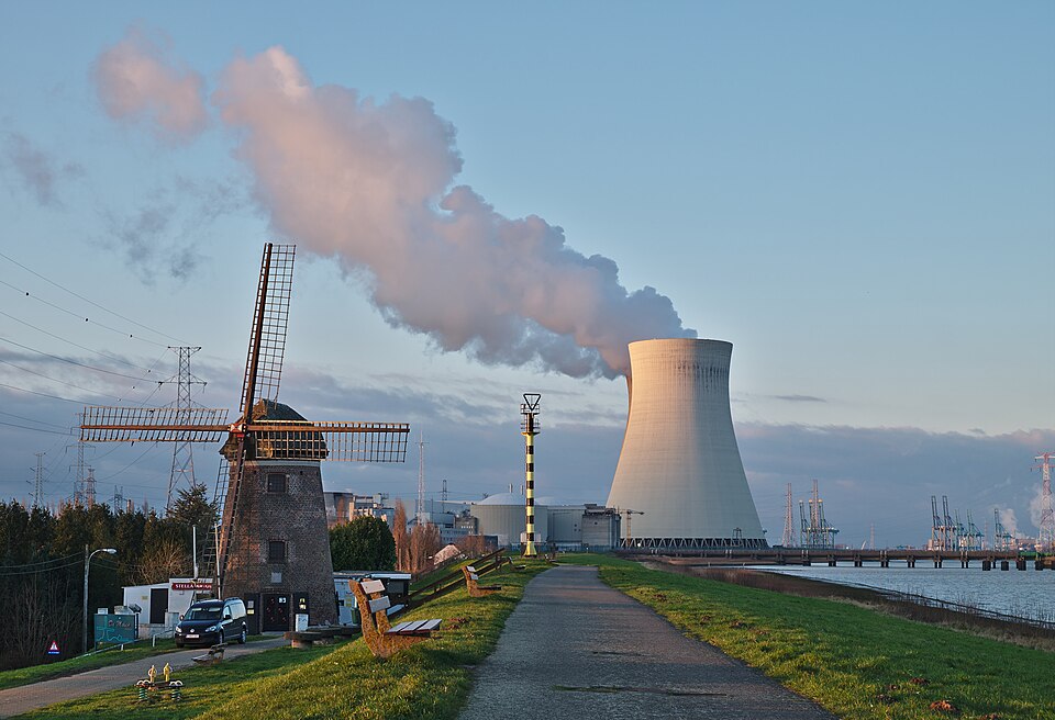 Nuclear power plant cooling tower emitting steam with reactor buildings at Doel