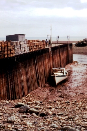 Boat grounded on exposed seabed beside a tall tidal pier at low tide in the Bay of Fundy