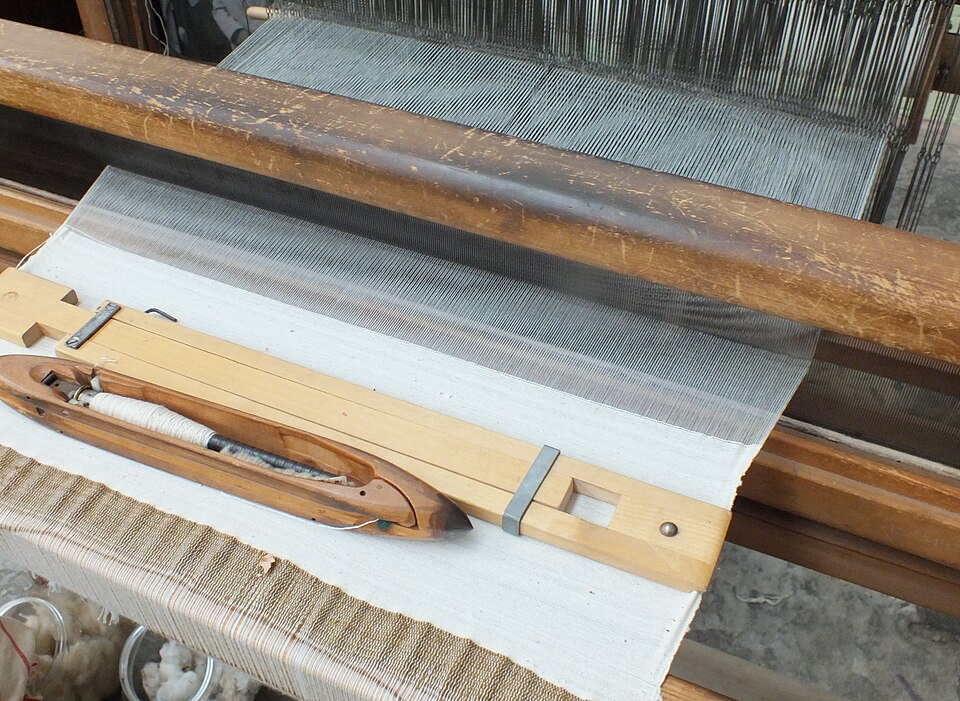 Wooden boat-shaped flying shuttle resting on cloth in a hand weaving loom
