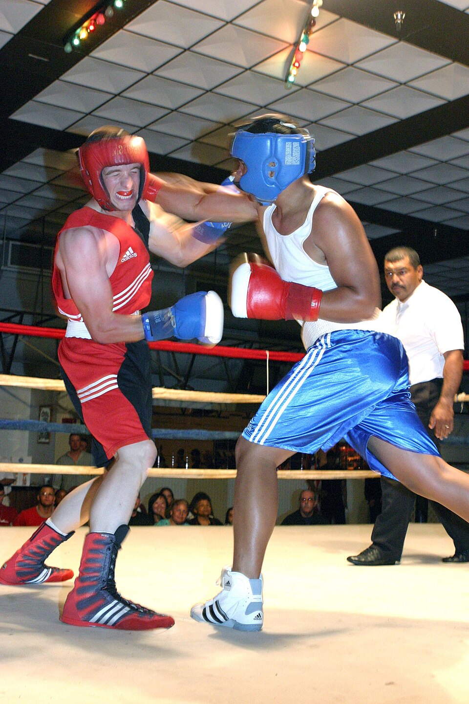 Two amateur boxers in headgear trading punches with gloves inside a boxing ring as a referee watches