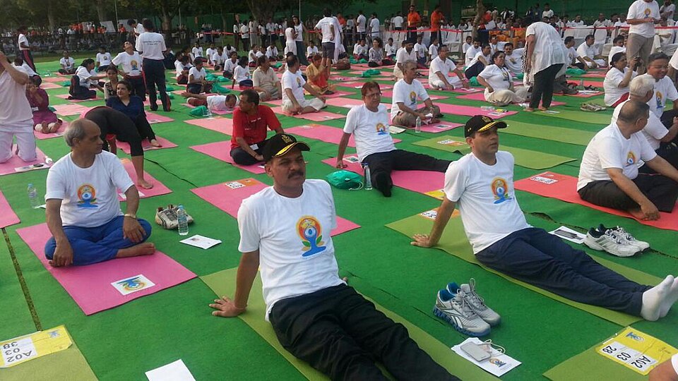 Rows of people seated on yoga mats performing an asana together at a mass International Day of Yoga session.