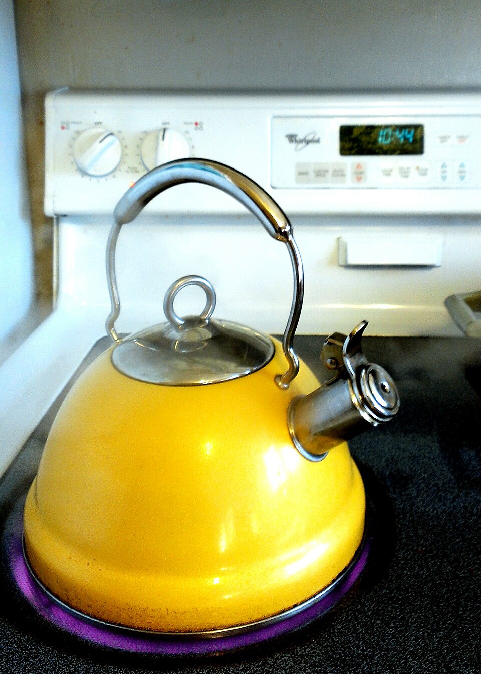 A yellow kettle heating water to a boil on a hot stovetop element