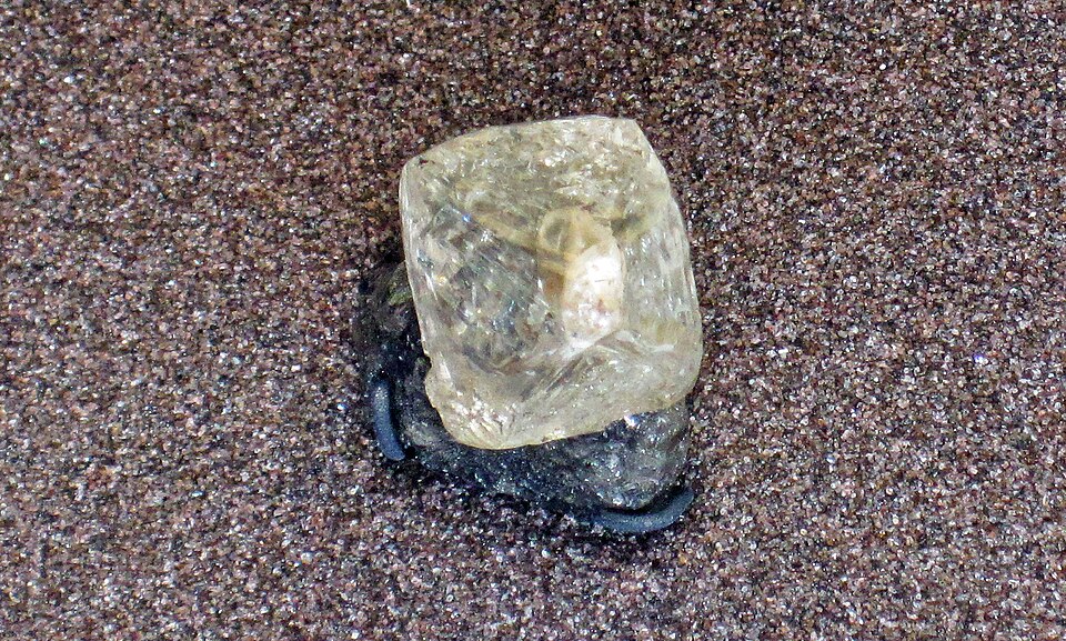 A natural translucent octahedral diamond crystal resting on sand