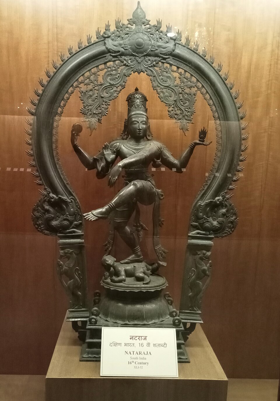A cast bronze Nataraja from South India on a museum plinth, the dancing figure ringed by a flaming arch, with the museum's label below it.