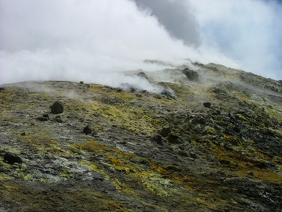 Steam escaping from fumaroles on the flank of Mount Etna, with patches of yellow sulphur crust coating the dark volcanic rock and ash around the vents.