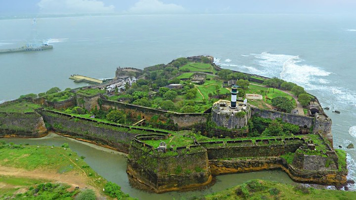 Aerial view of Diu Fort, a bastioned Portuguese-era stone fortress with a moat and a lighthouse, standing on a headland surrounded by the sea on Diu island.