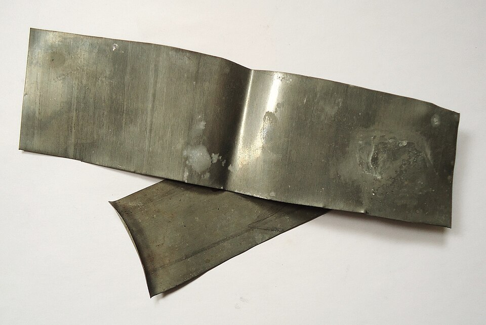 Two dull silver-grey sheets of zinc metal lying on a plain white surface.