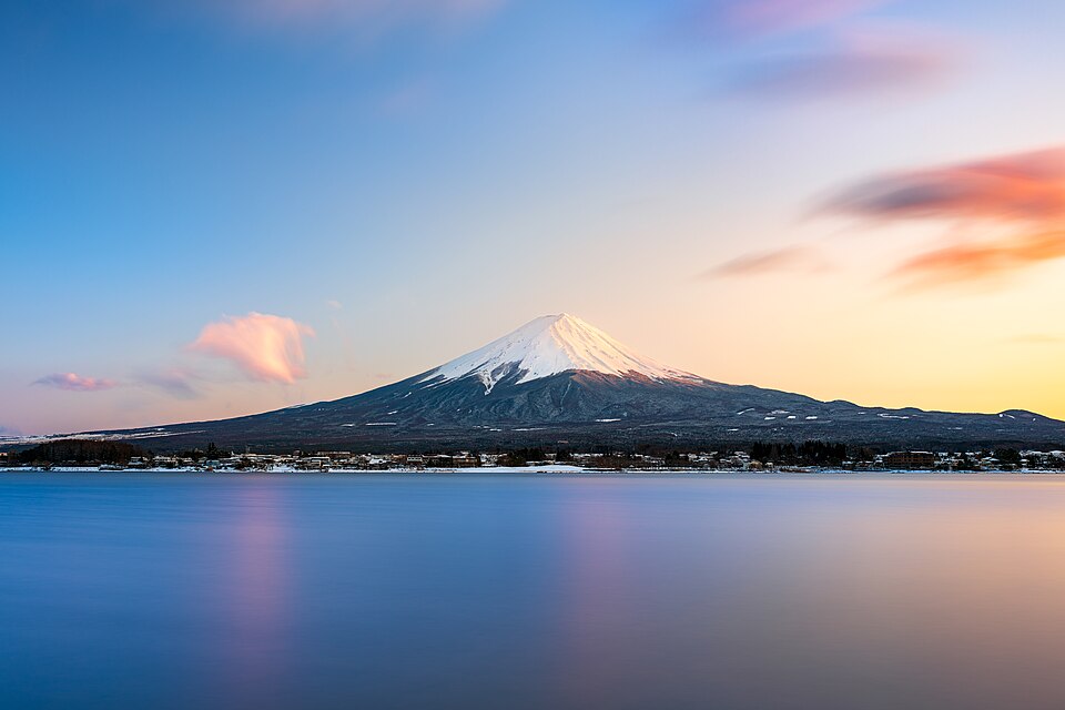 Mount Fuji at sunset, a near-symmetrical snow-capped volcanic cone rising above a lake that mirrors it.