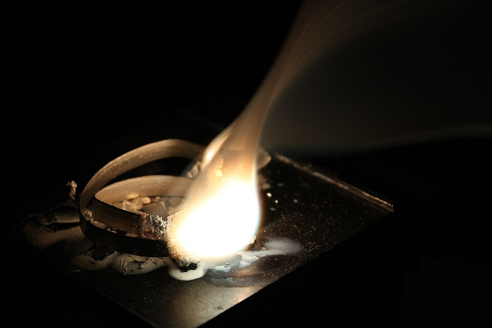 A coil of magnesium ribbon burning on a metal plate with an intense white flame, leaving a residue of white magnesium oxide powder.