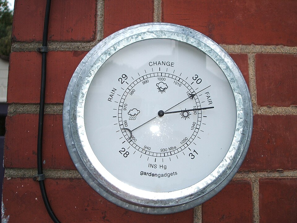 A round wall-mounted aneroid barometer, its dial marked RAIN, CHANGE and FAIR with an inner scale reading in millibars and an outer scale in inches of mercury.
