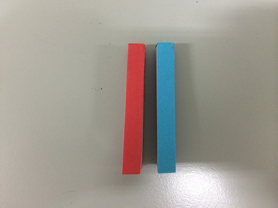A red litmus paper strip and a blue litmus paper strip lying side by side on a plain pale surface.